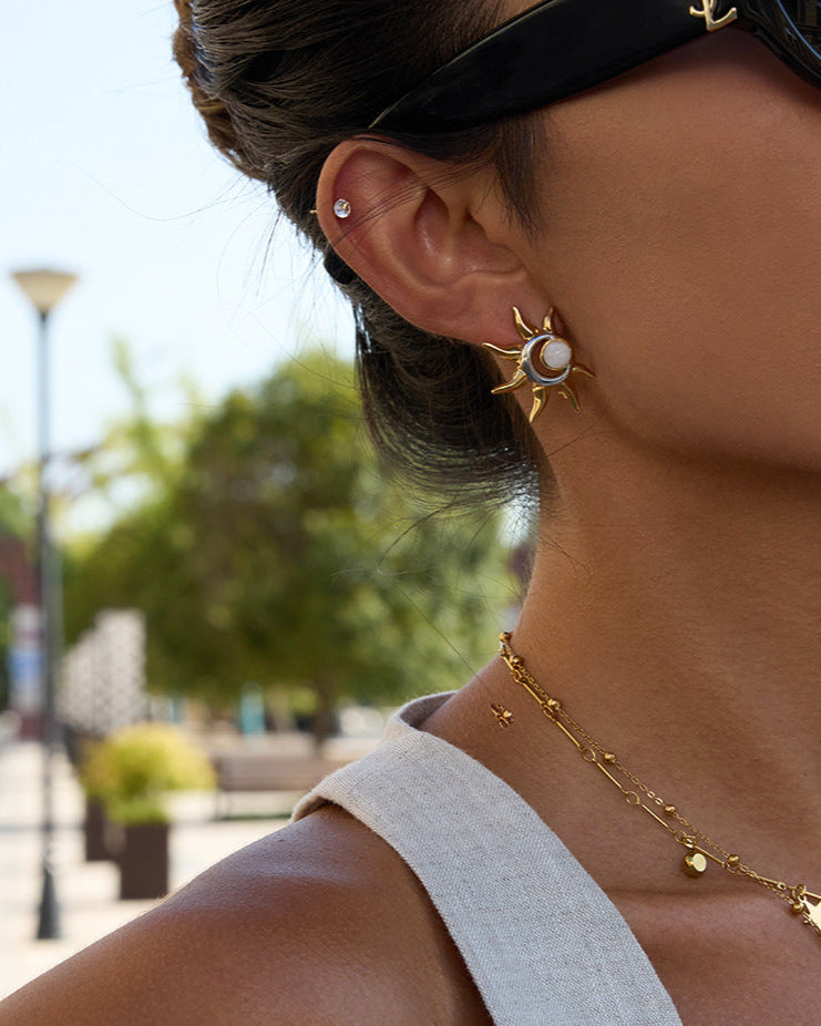 Woman wearing gold necklaces and earrings with a blurred outdoor background