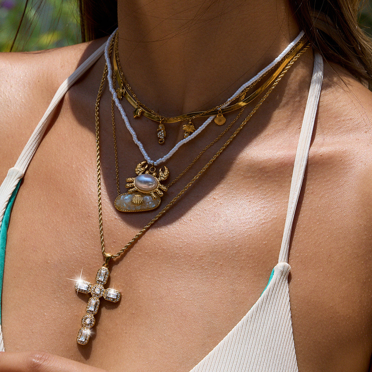 Layered necklaces styled with crab and cross pendants on beach-ready outfit