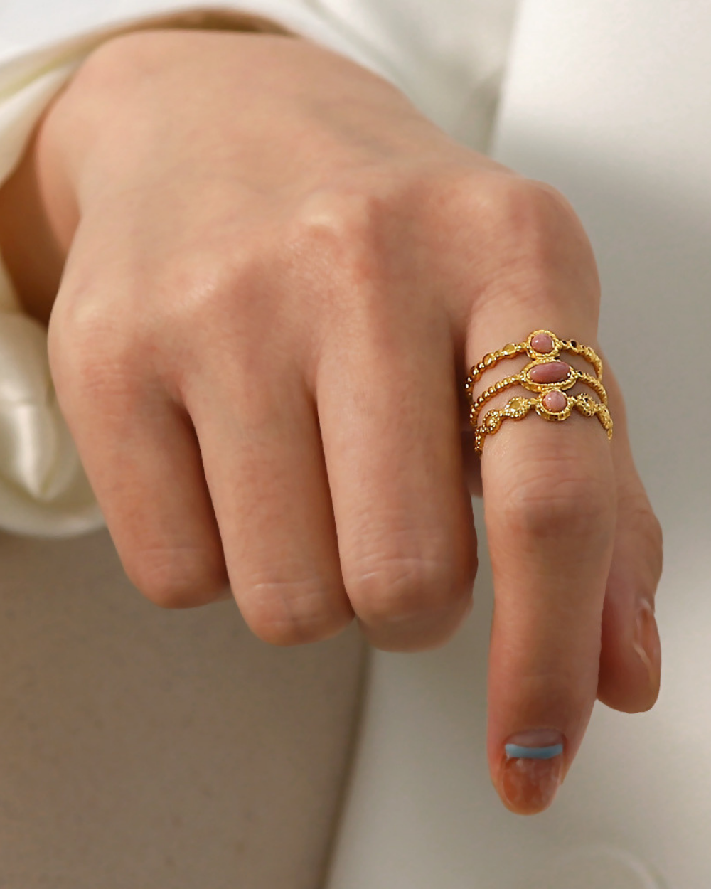 Close-up of a hand wearing gold rings with pink stones on a neutral background