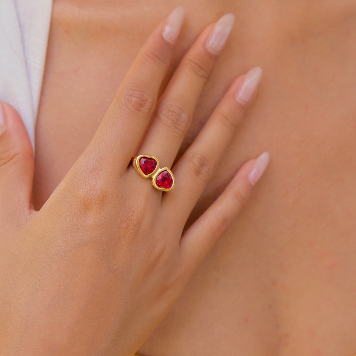 Woman’s hand wearing a gold double-heart gemstone ring in daylight