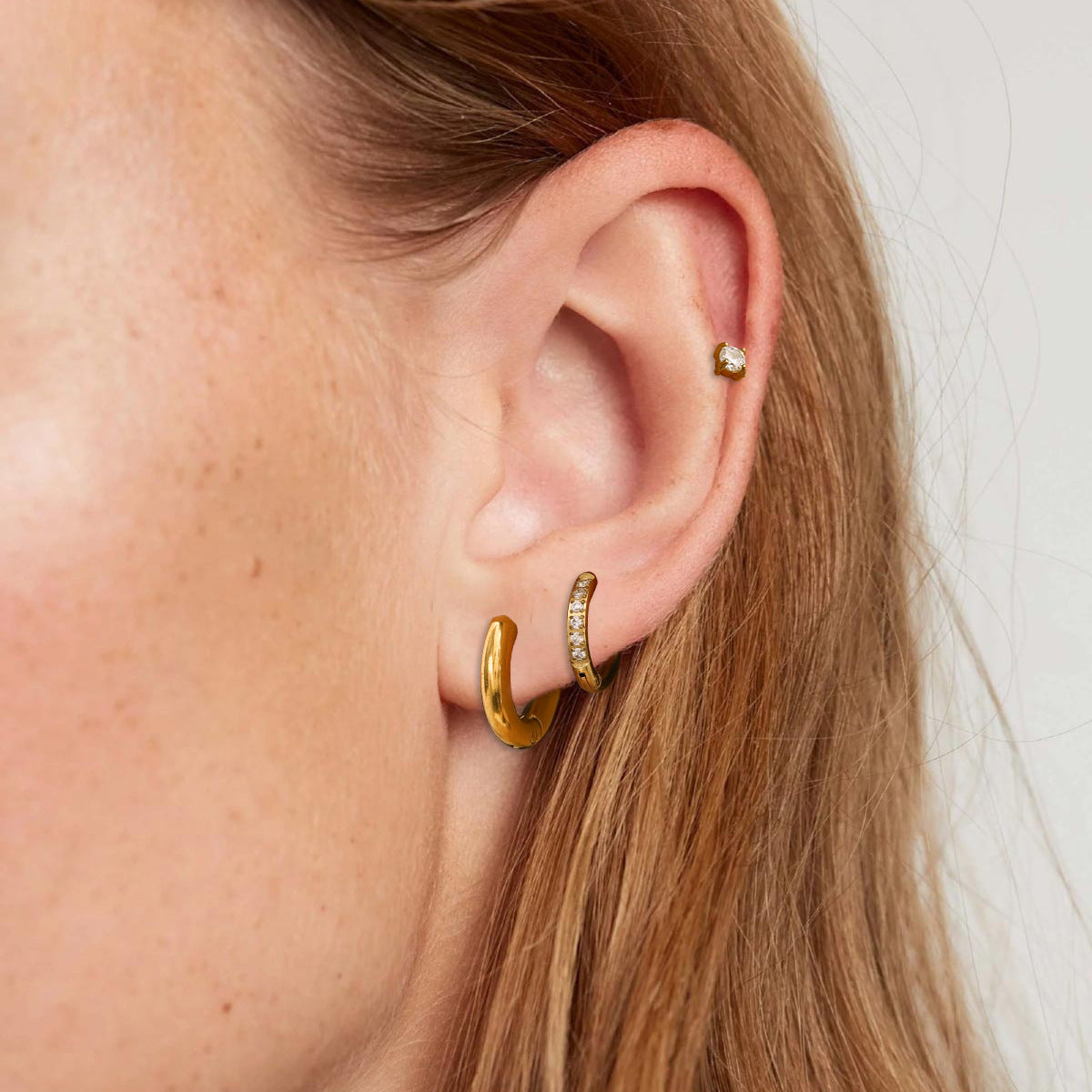 Model wearing a mix of hoop and stud earrings in a triple-piercing style, close-up ear view.