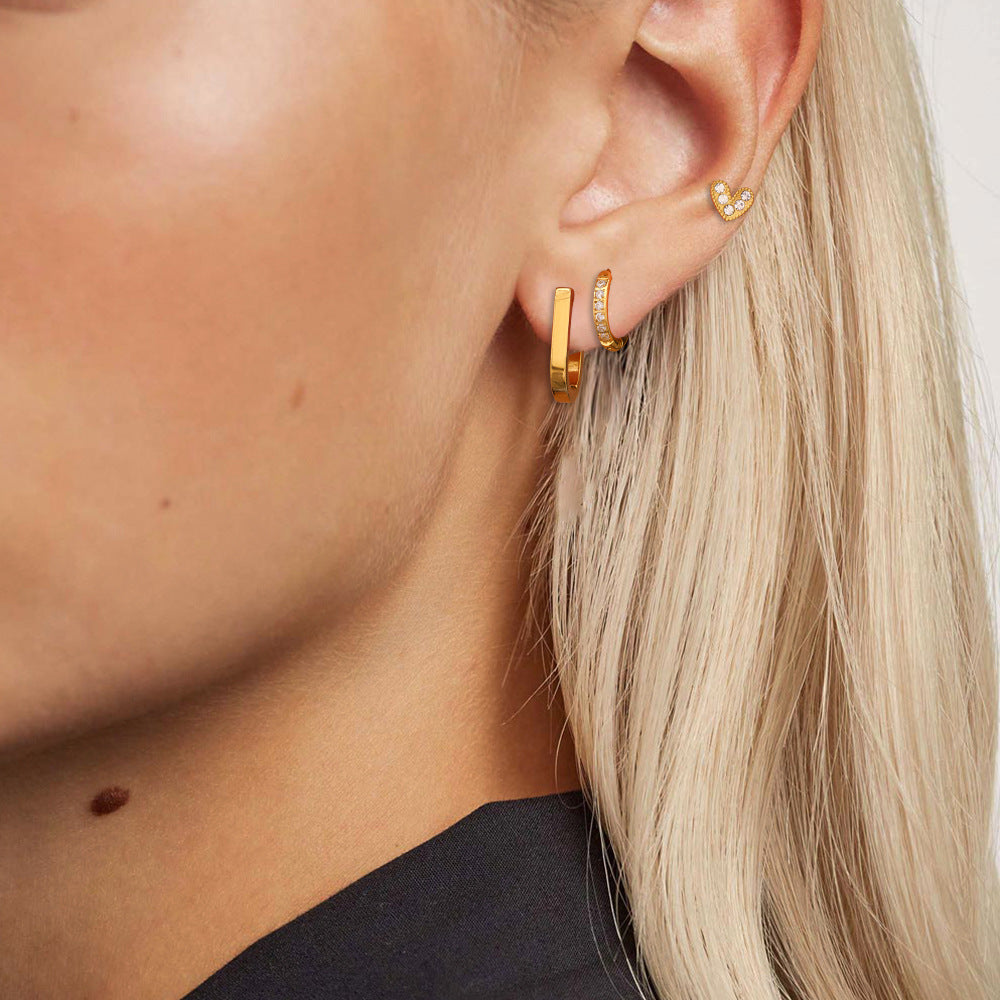 Model wearing layered gold earrings with heart studs and two types of hoops for chic styling