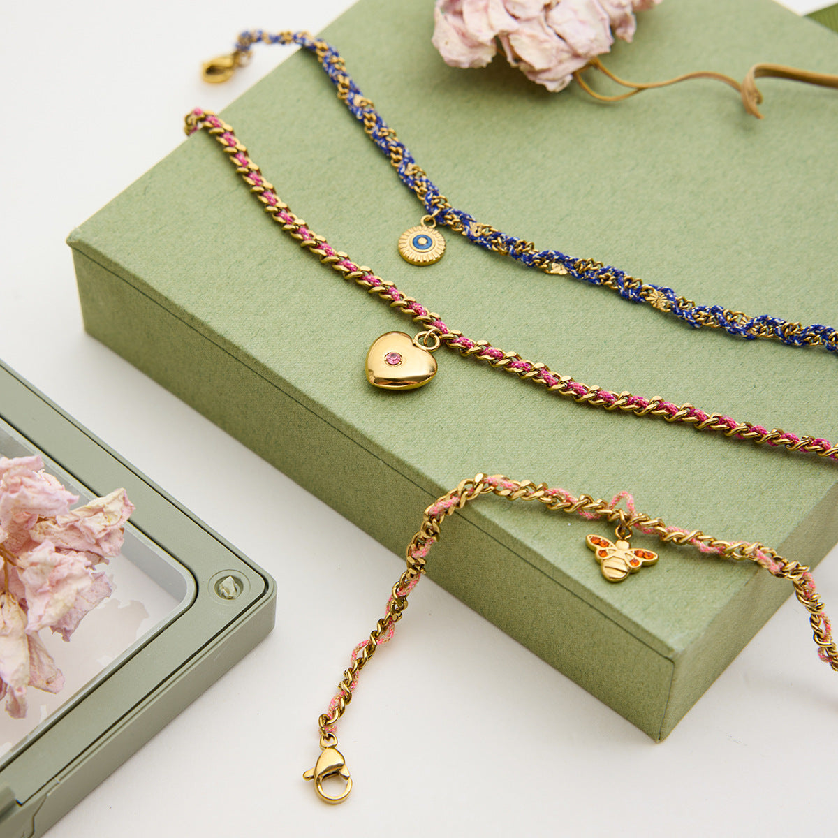 Three braided necklaces with charms on a green jewelry box with pink flowers.