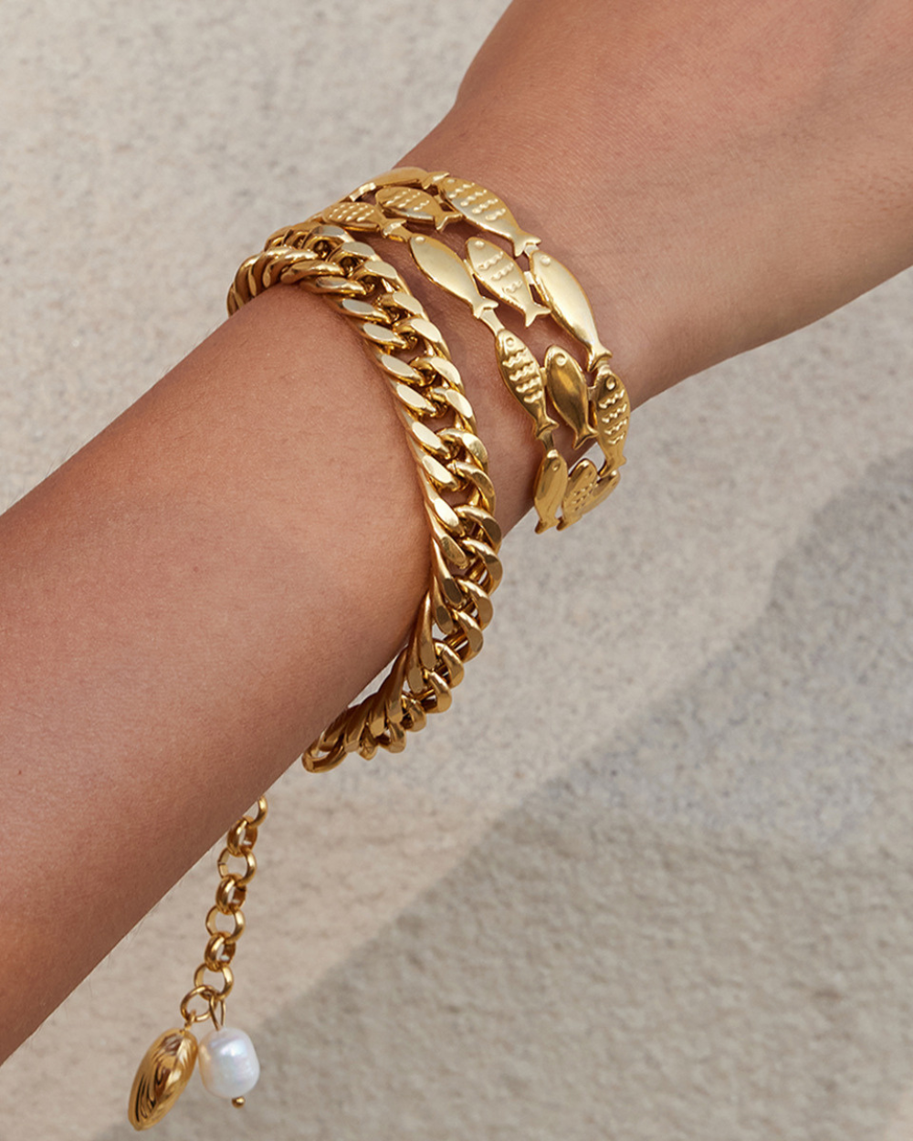 Gold bracelet with leaf design on a wrist against a neutral background