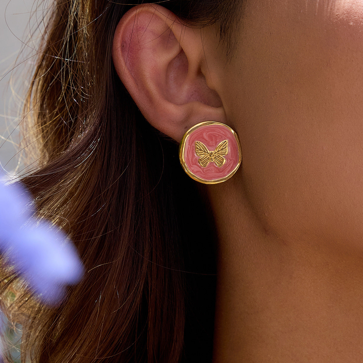 Model wearing gold butterfly stud earrings with pink enamel swirl