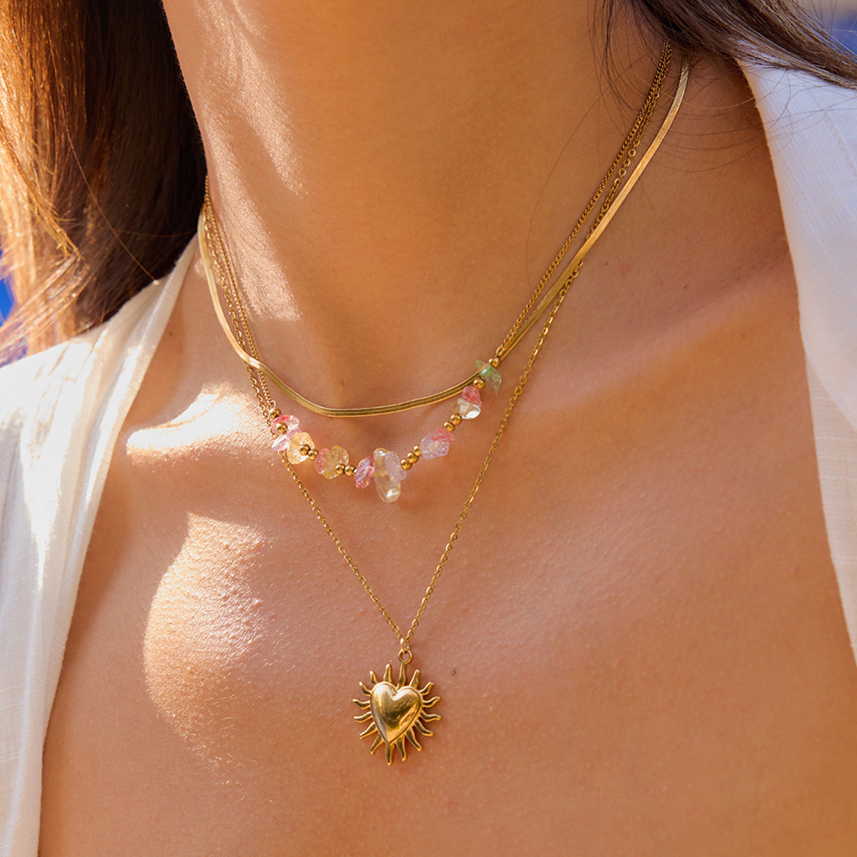 Woman wearing layered heart pendant necklace under sunlight