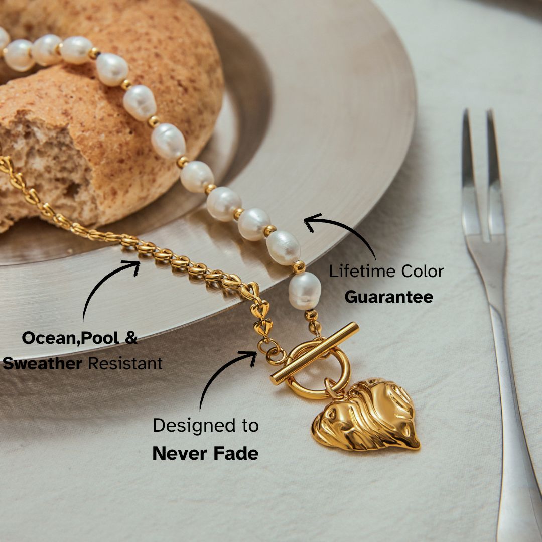 Elegant gold heart pendant and freshwater pearl necklace styled on a modern table setup with bagel and silver cutlery