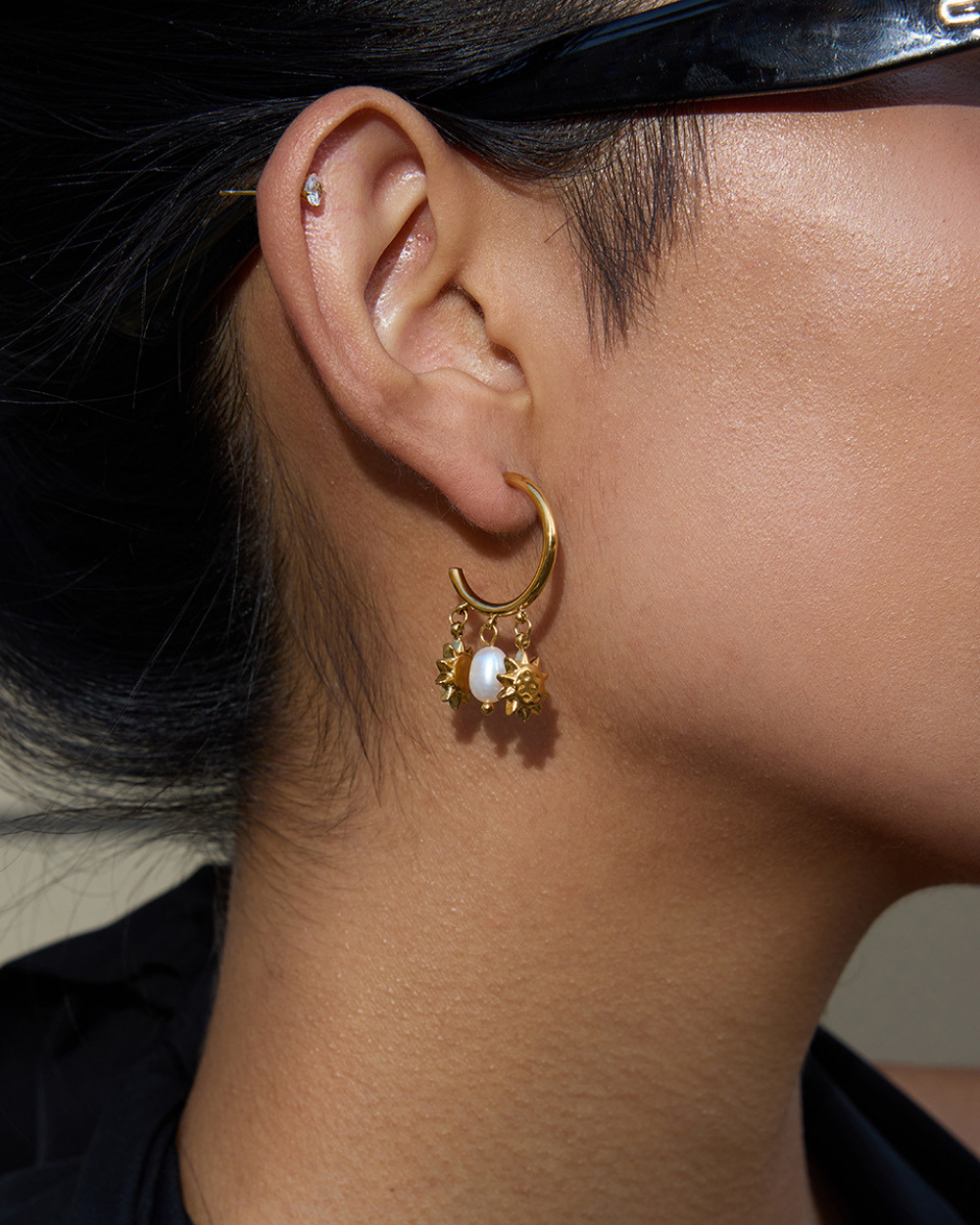 Close-up of an ear wearing a gold earring with a pearl pendant.
