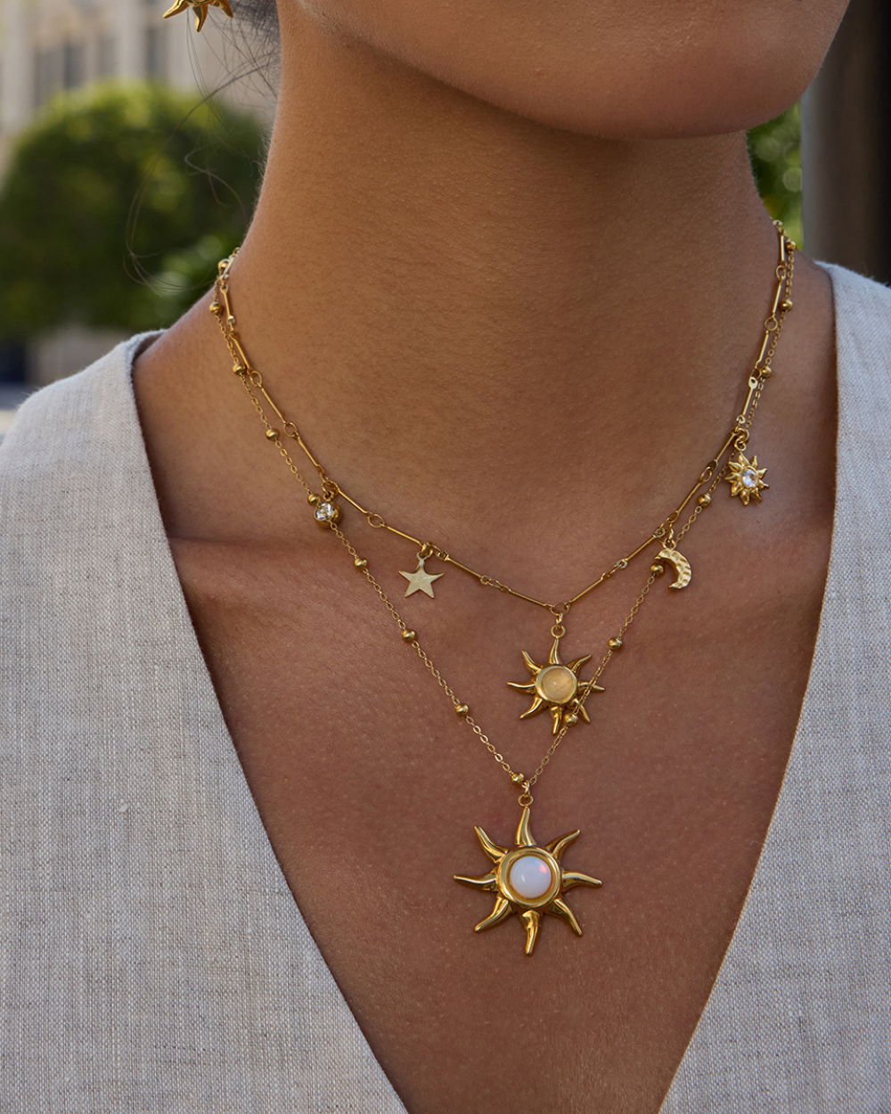 Gold necklace with sun and moon pendants on a person wearing a light gray cardigan.