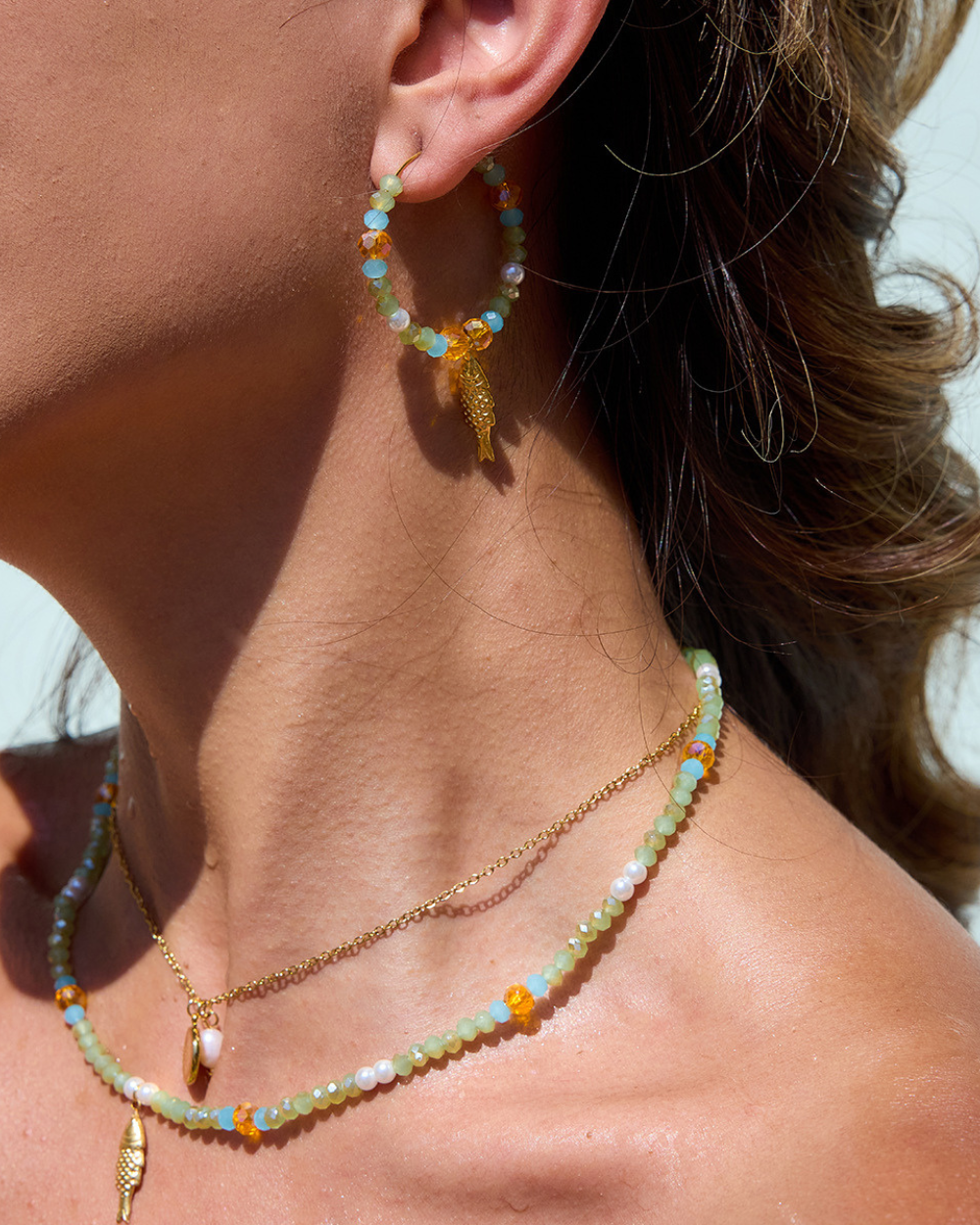 Close-up of a person wearing colorful beaded earrings and necklaces.