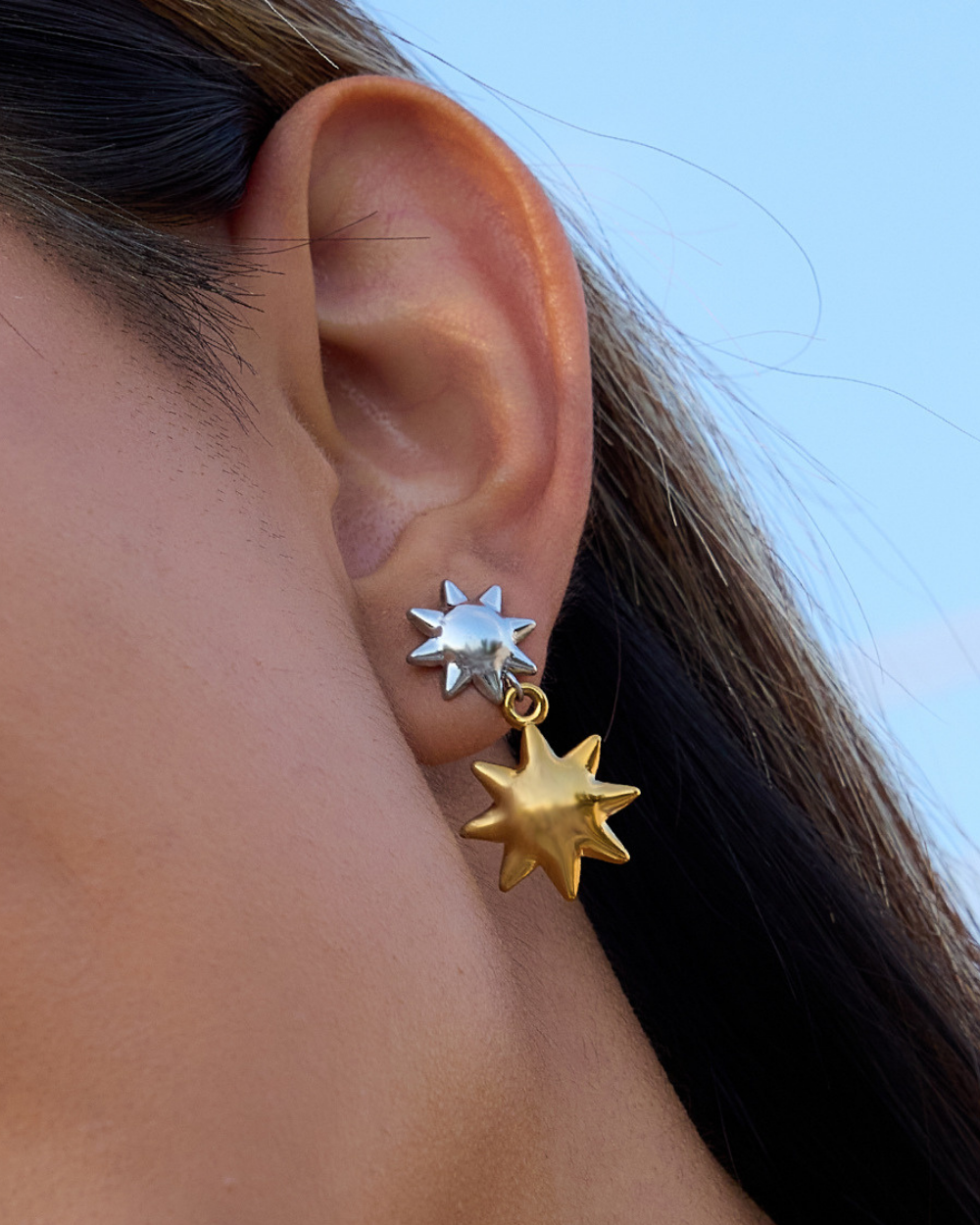 Close-up of a person wearing gold and silver star-shaped earrings.