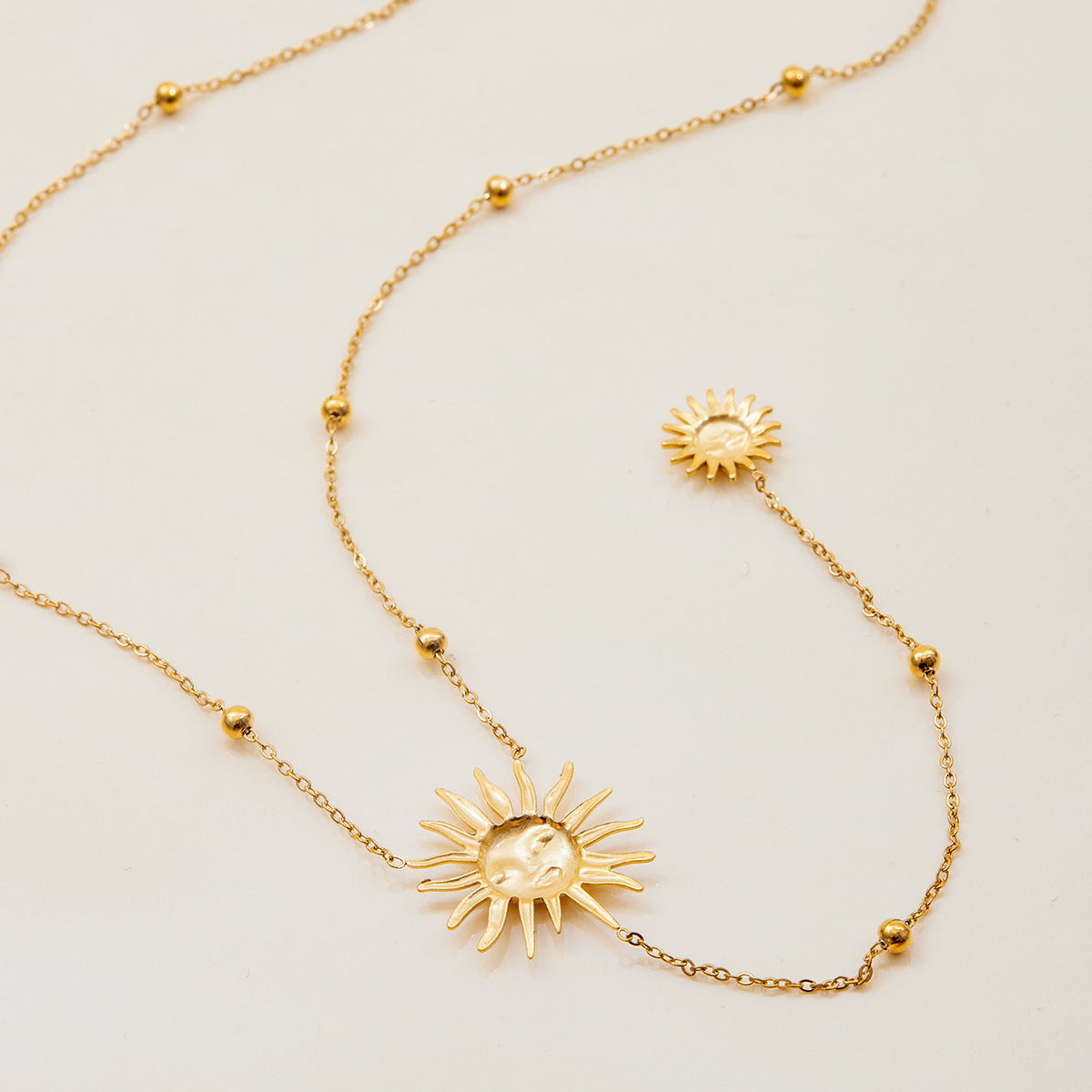 Gold necklace with sun-shaped pendants on a light beige background