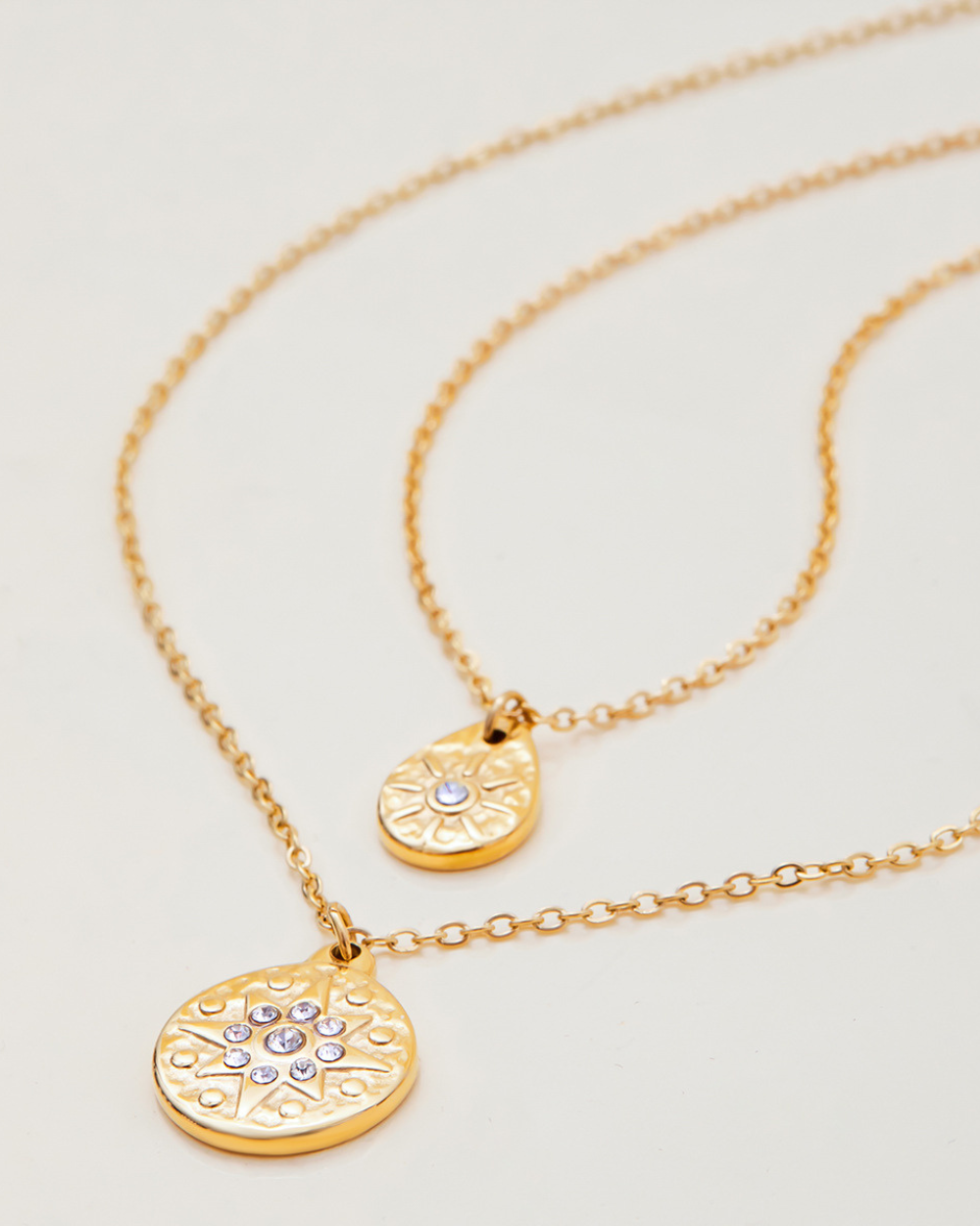 Two gold necklaces with circular pendants on a light gray background