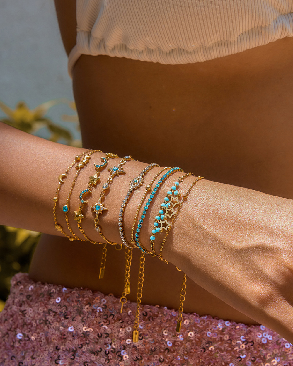 Close-up of a wrist wearing multiple gold and turquoise bracelets against a blurred background.