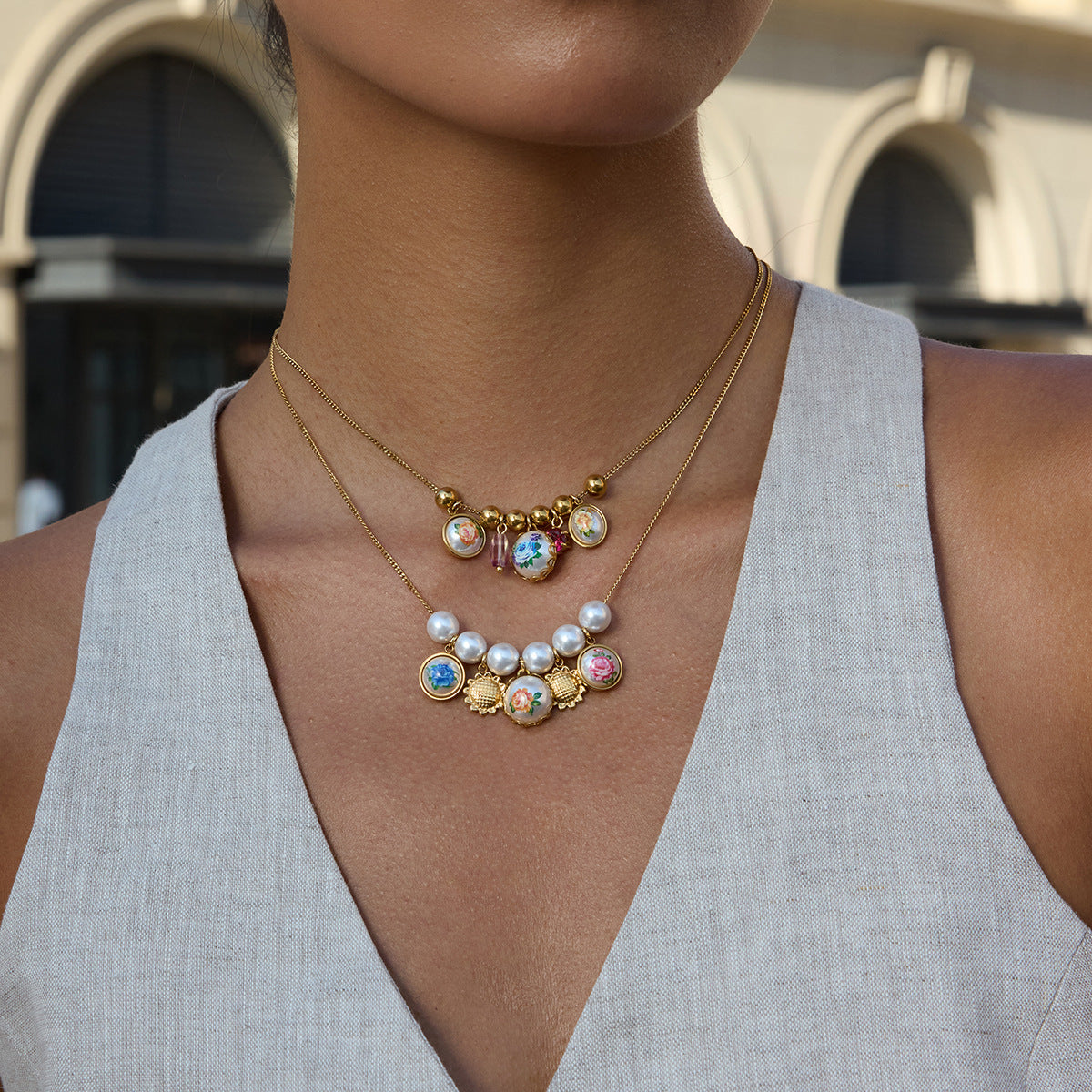 Woman wearing a gold necklace with colorful charms and pearl accents.