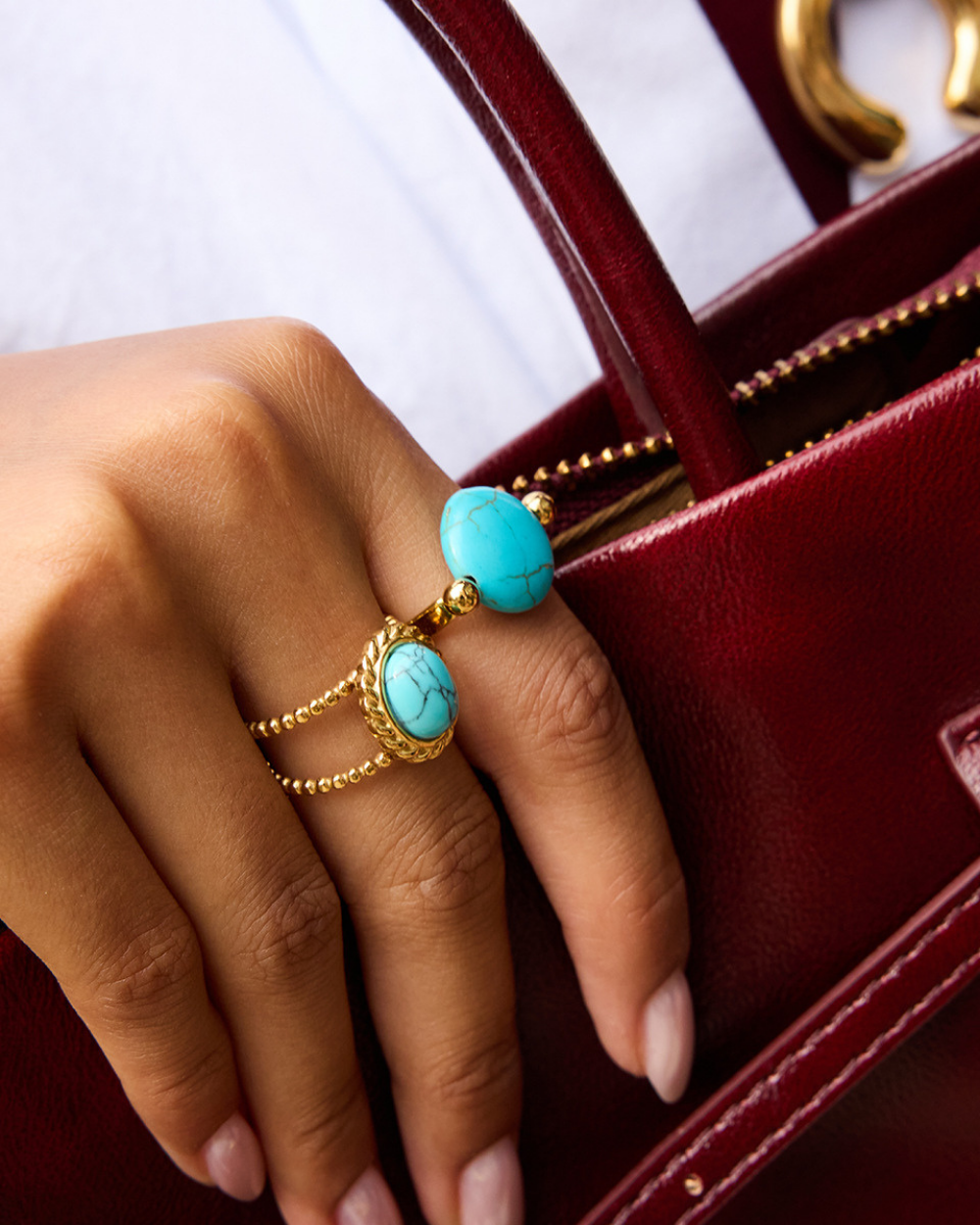 Hand wearing gold rings with turquoise stones against a red background
