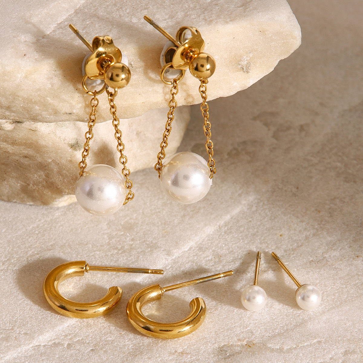Elegant gold and pearl drop earrings set styled on stone surface for chic everyday wear
