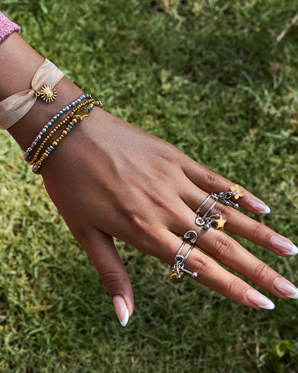 Hand wearing multiple bracelets and rings on a grass background