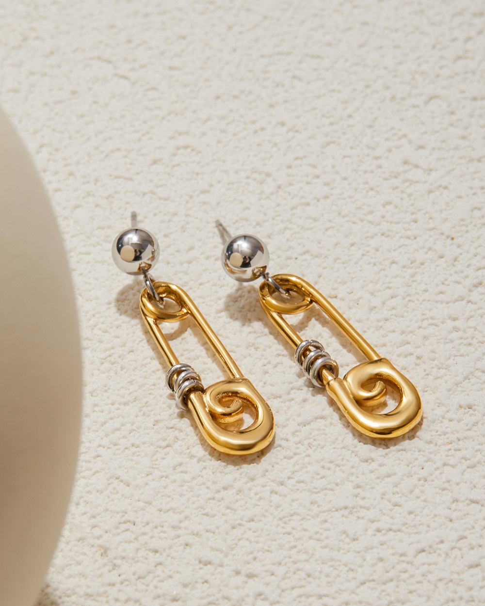 Gold and silver earring on a textured beige surface