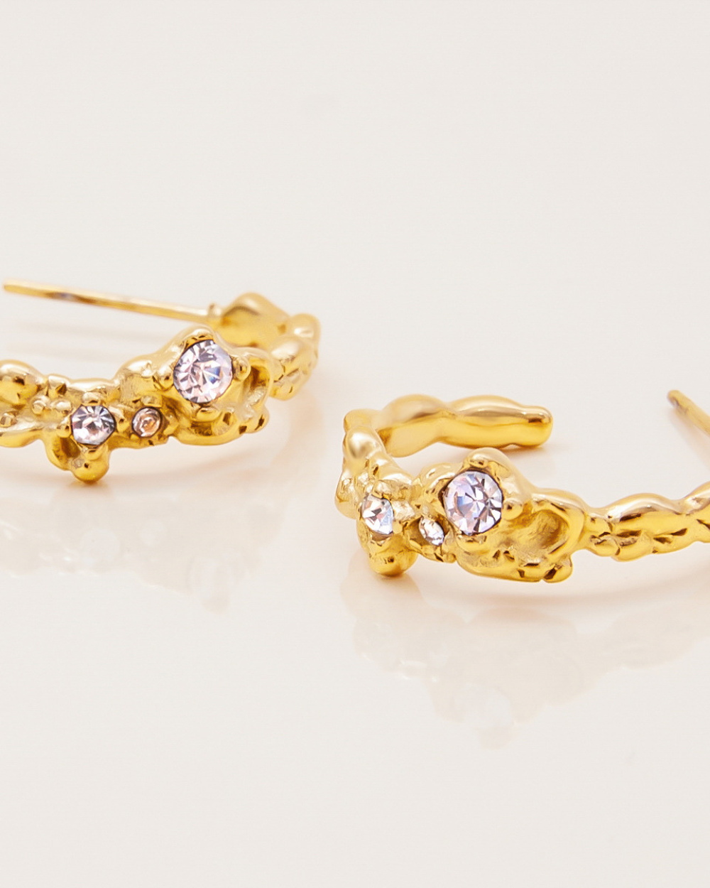Gold earrings with crystal stones on a light beige background