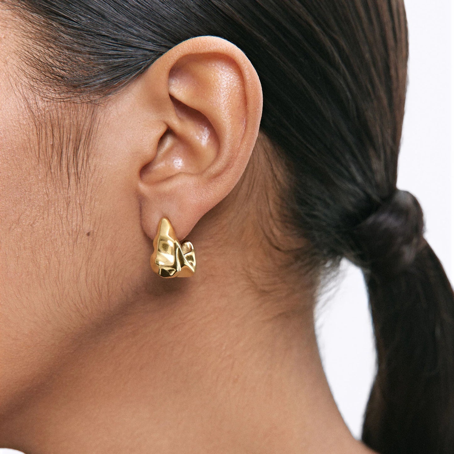 Woman wearing abstract gold sculpted hoop earrings with hair tied back