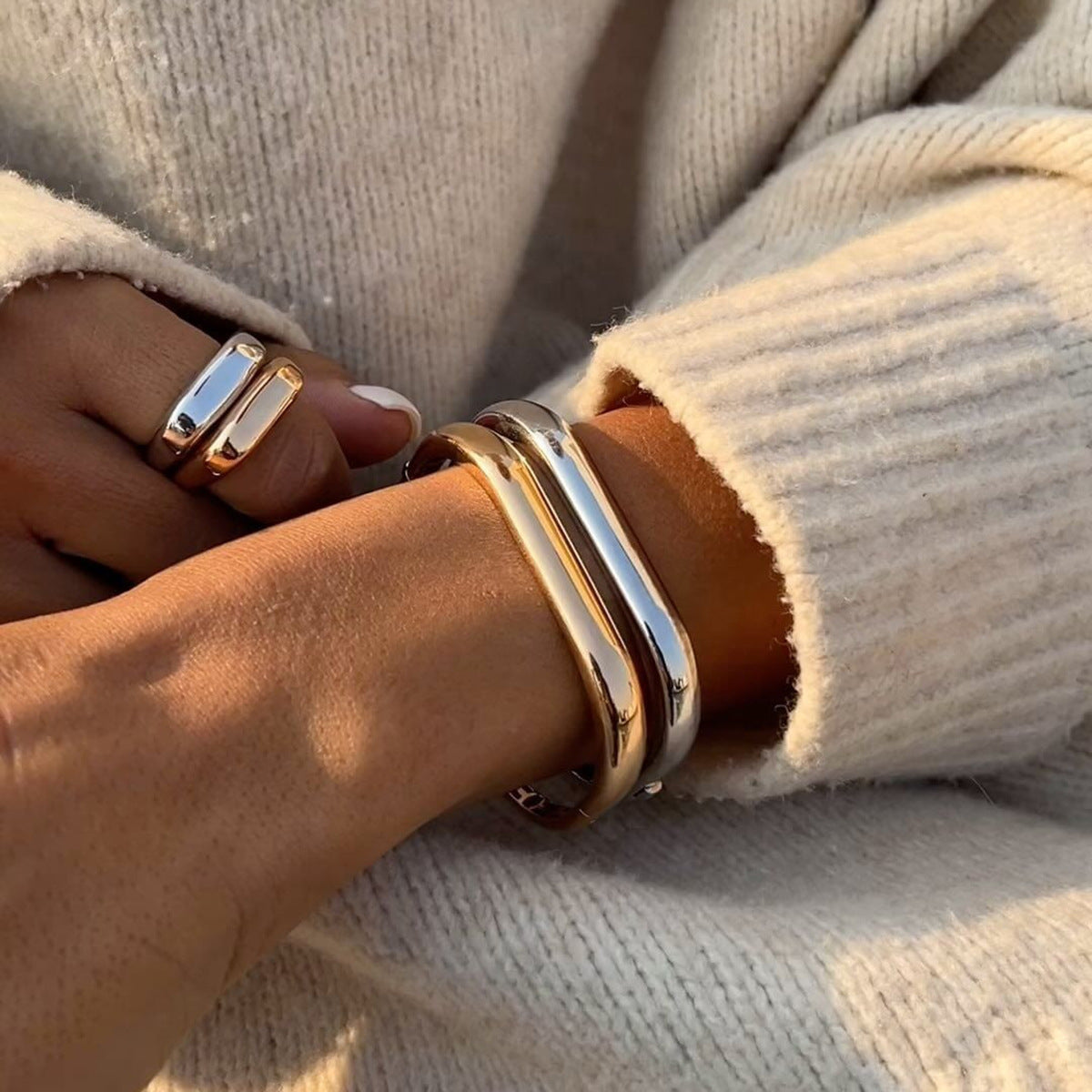 Gold and silver bangle bracelet styled with a cream knit sweater in warm sunlight