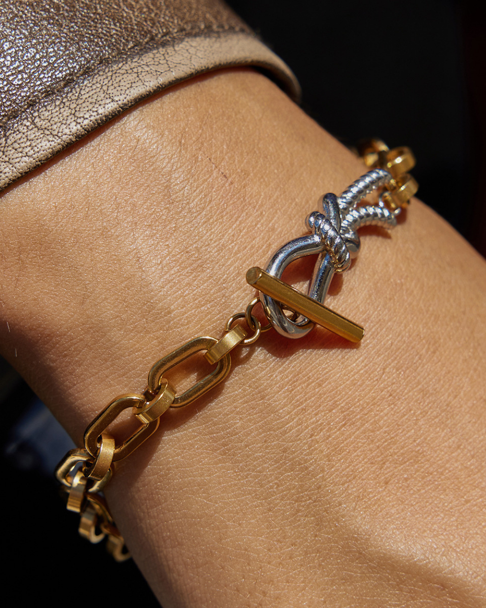 Gold and silver bracelet on a wrist with a dark background