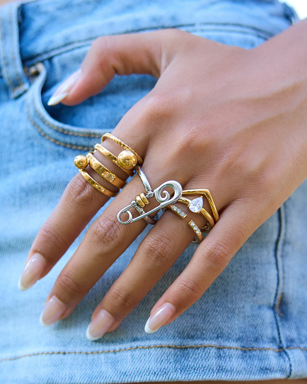 Hand wearing multiple gold and silver rings on a denim background
