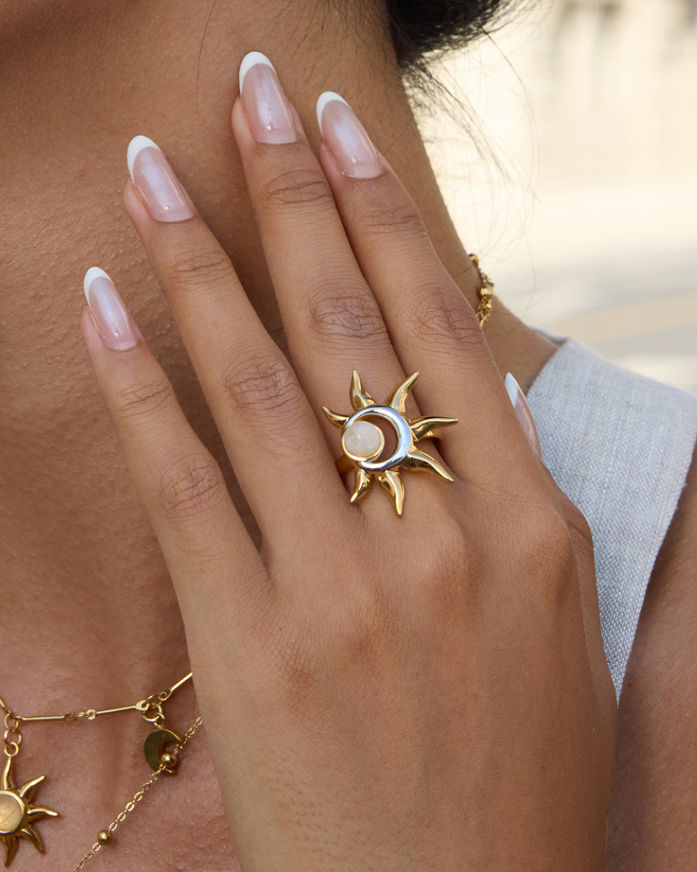 Hand wearing a gold ring with sun design, close-up shot.