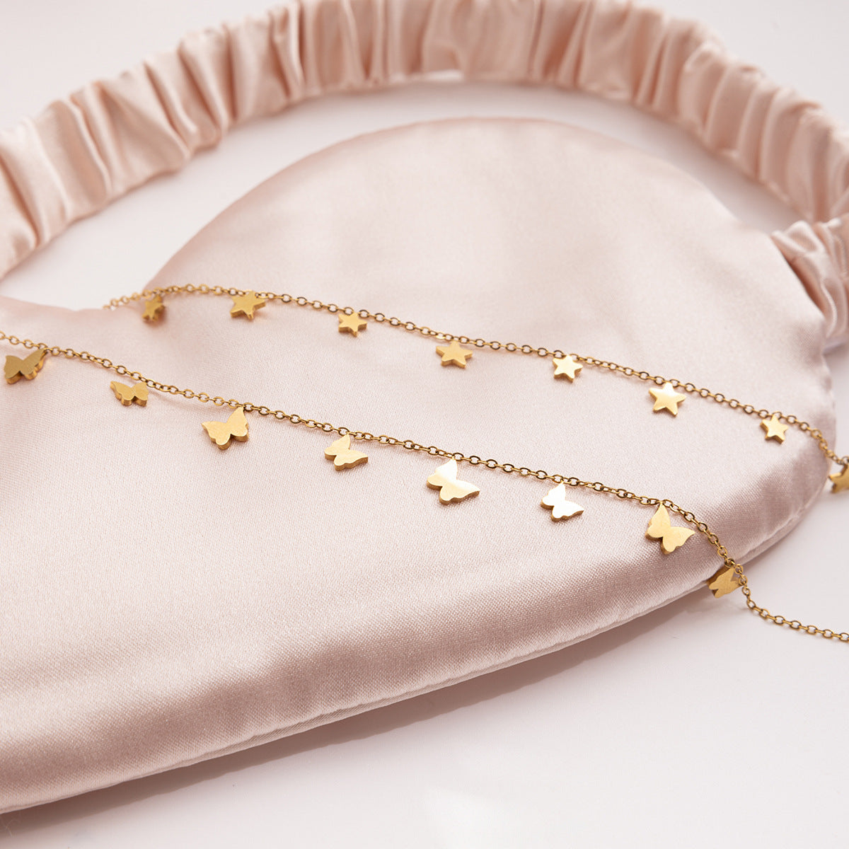 Gold necklace with heart and star pendants on a pink velvet surface