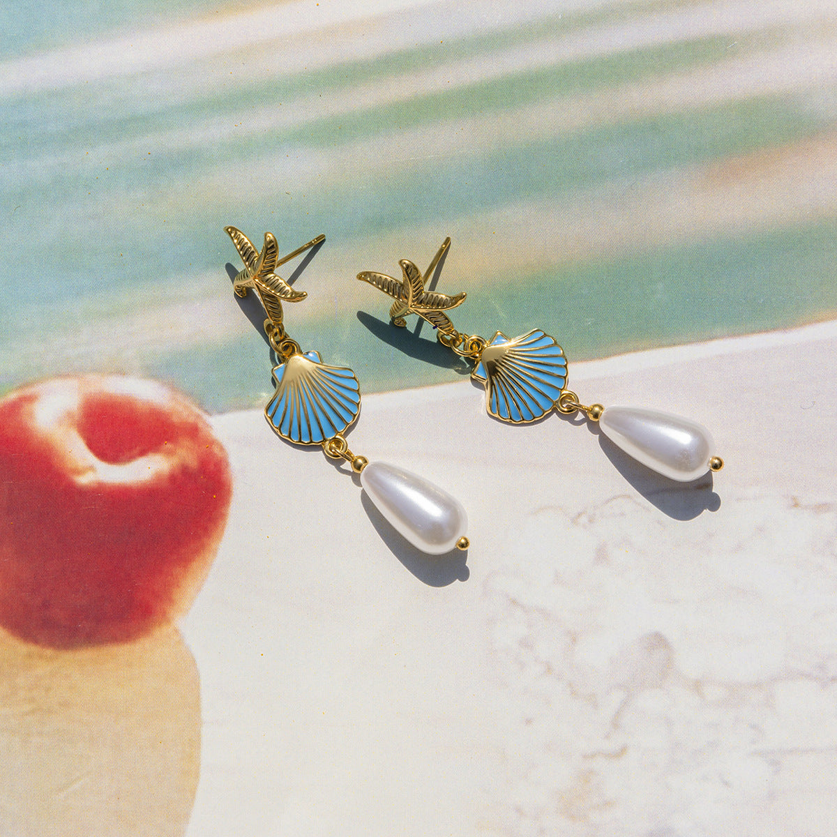 Gold starfish earrings with blue shell charms and pearl drops on textured backdrop