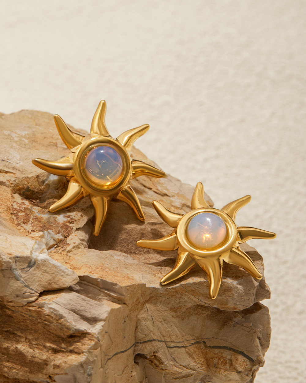 Gold sun-shaped earrings with gemstones on a stone surface