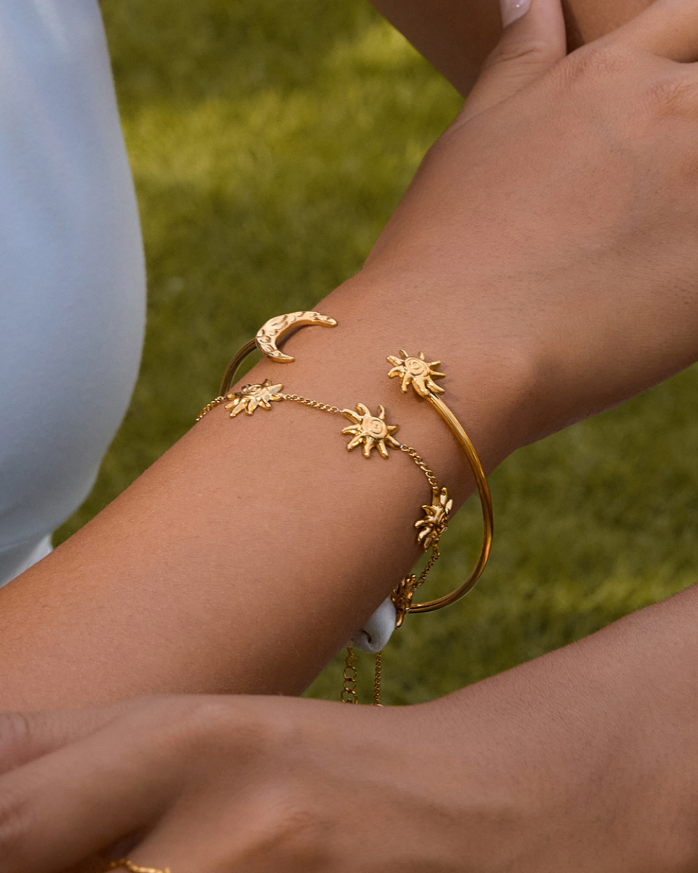 Gold bracelet with star and moon designs on a wrist against a grassy background
