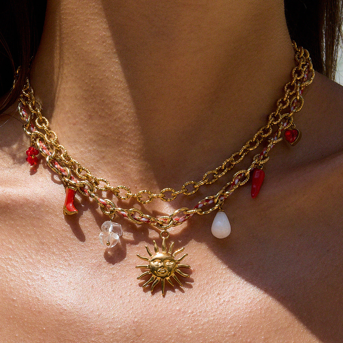 Gold chain necklace with sun charm and red and clear beads on a person's neck.