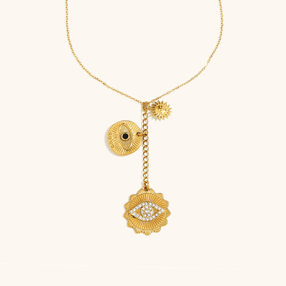 Gold necklace with sun, eye, and crystal charms on cream fabric