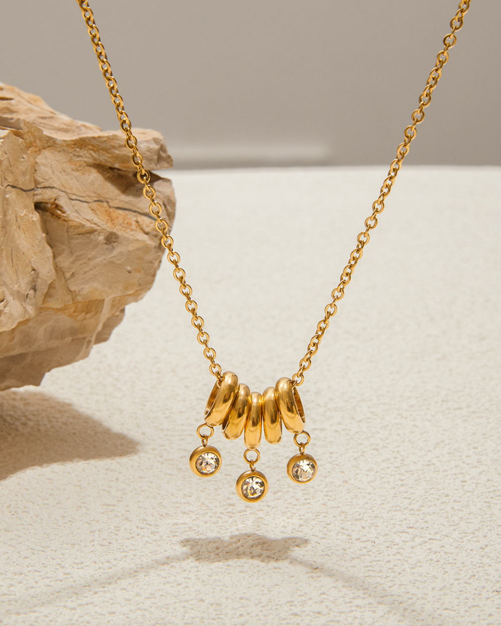 Gold necklace with three hanging charms on a neutral background