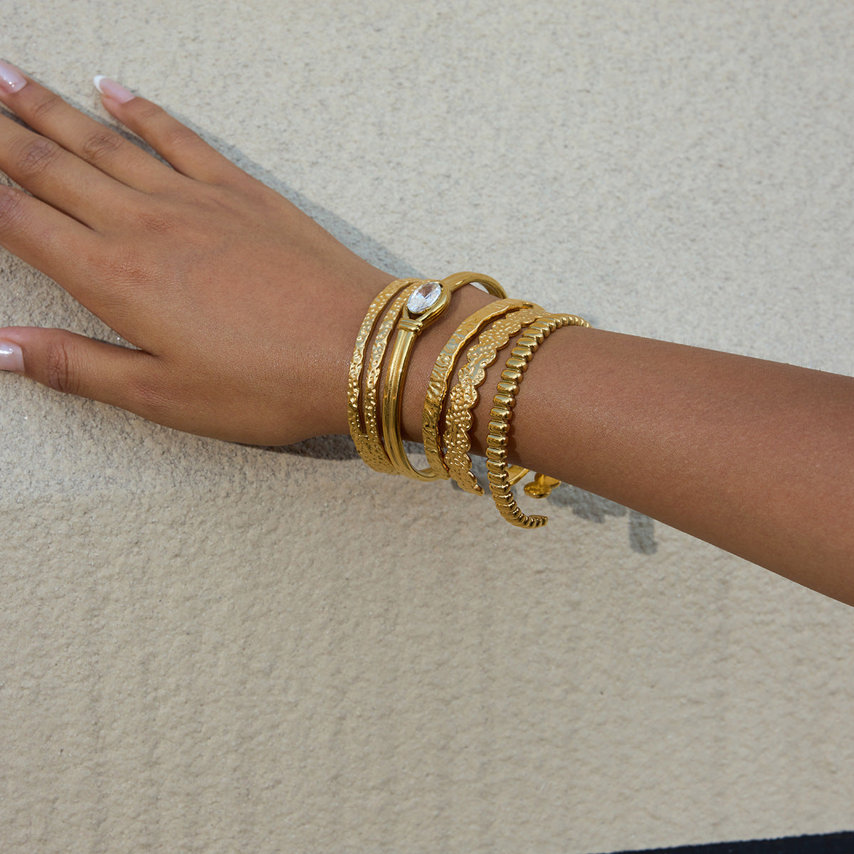 Hand wearing multiple gold bracelets on a neutral background