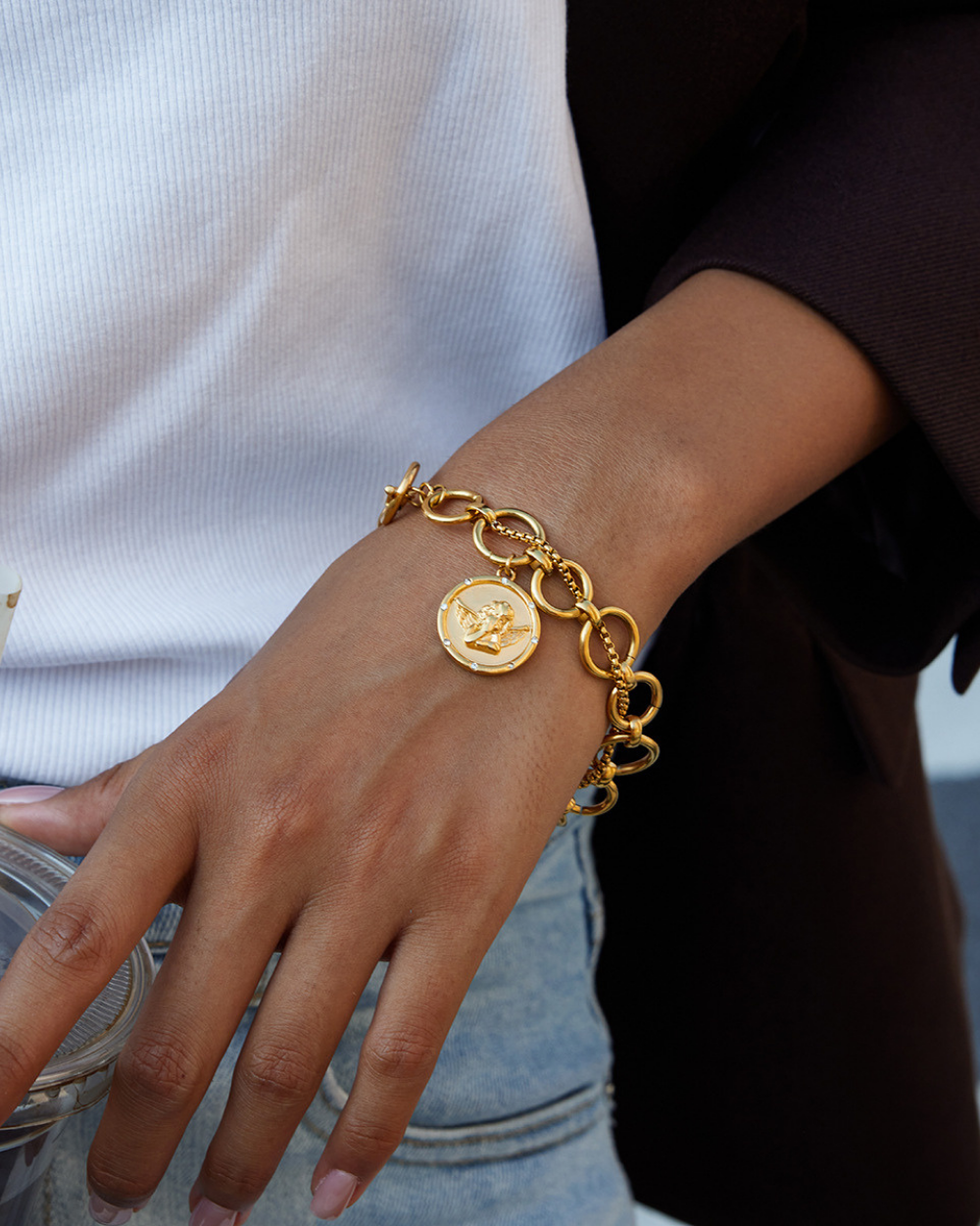Gold bracelet with circular charm on a wrist against a neutral background