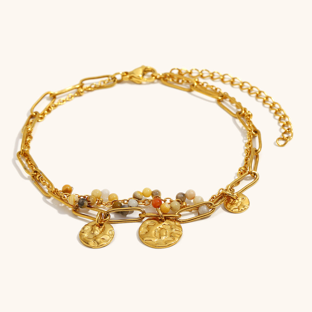 close-up of gold coin charm layered bracelet on cream background