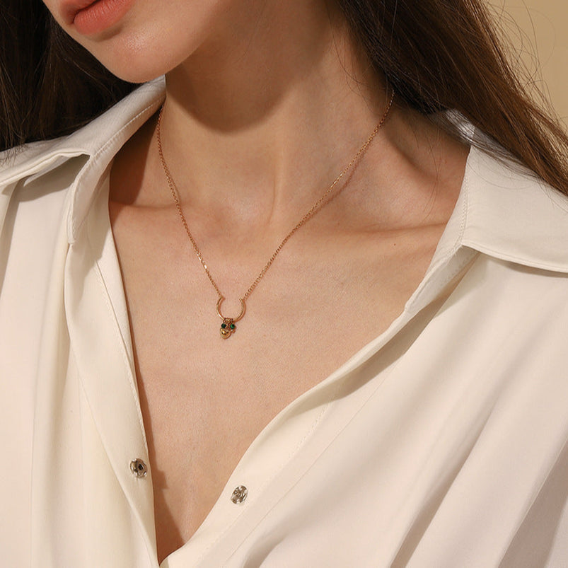 Woman wearing a dainty gold heart necklace with green beads, close-up front view.