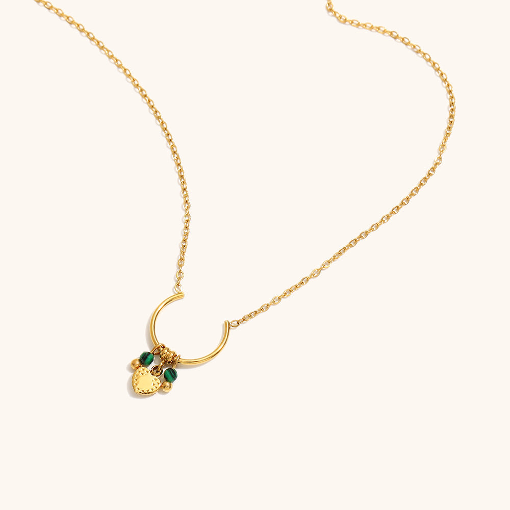 Close-up of gold U-shaped necklace pendant with textured heart and green stones.
