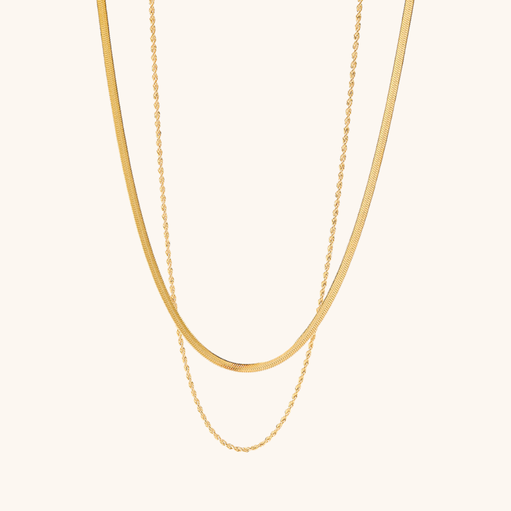 Close-up of double-layer gold necklace with rope and snake chains, styled on a neutral background