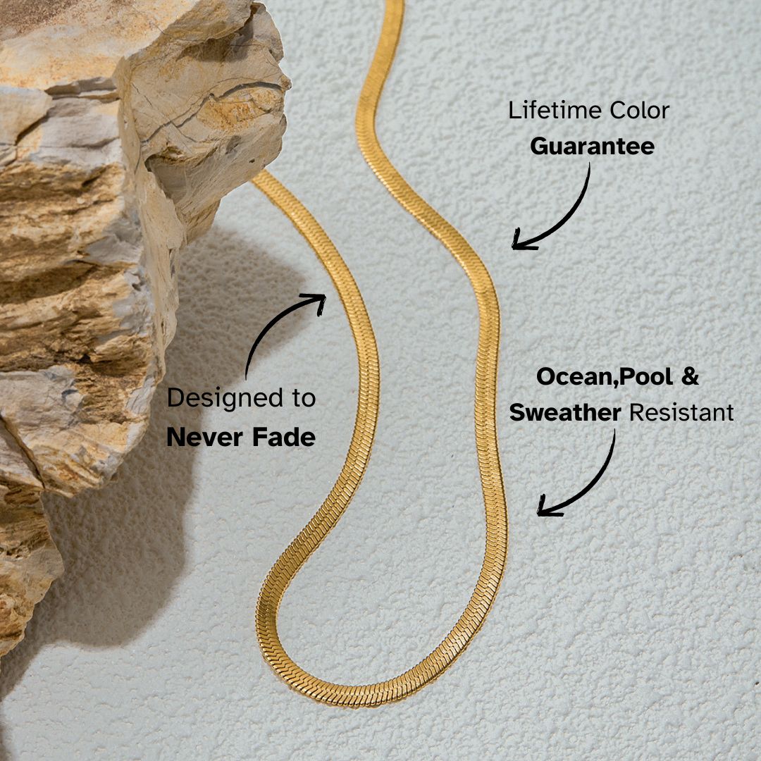 Flat gold snake chain necklace laid on textured stone, minimalist chic jewelry.