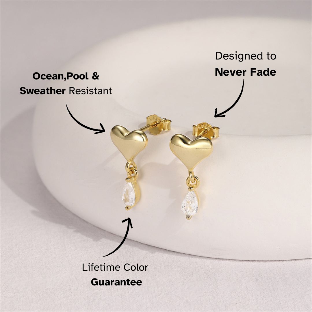 Gold heart drop earrings with clear crystal, displayed on marble tray