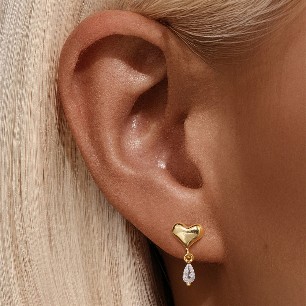 Close-up of woman wearing golden heart drop earrings with teardrop zircon