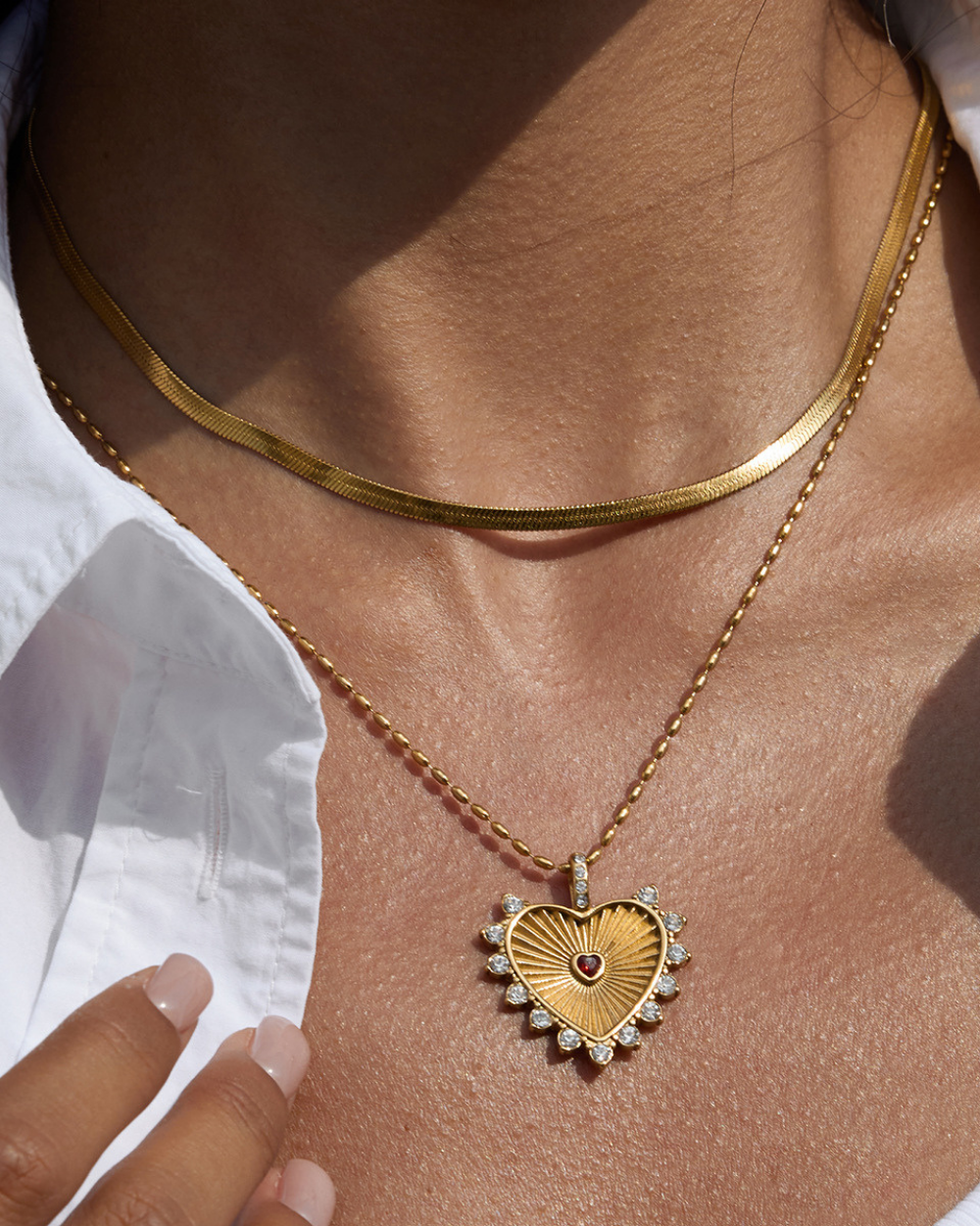 Gold necklace with a heart-shaped pendant on a person wearing a white shirt.