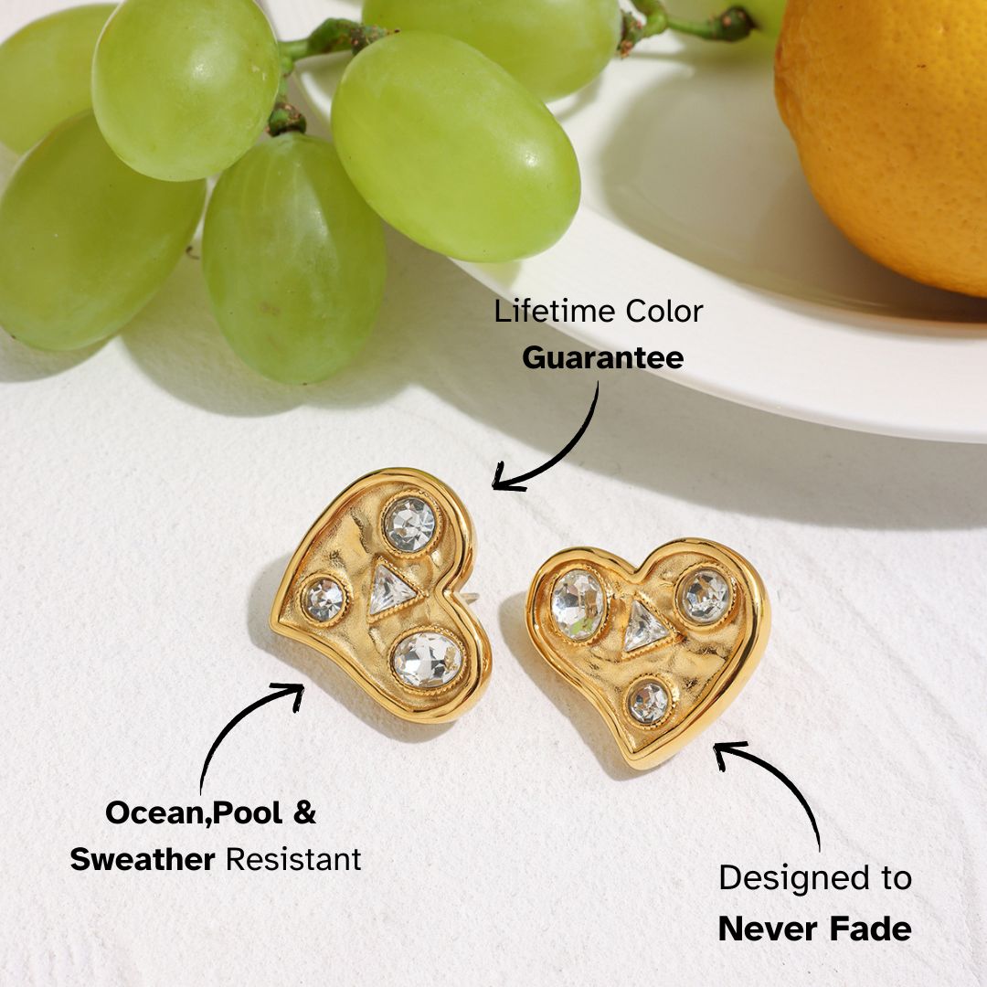Gold heart earrings with sparkling crystals placed on a white plate beside grapes and lemon.
