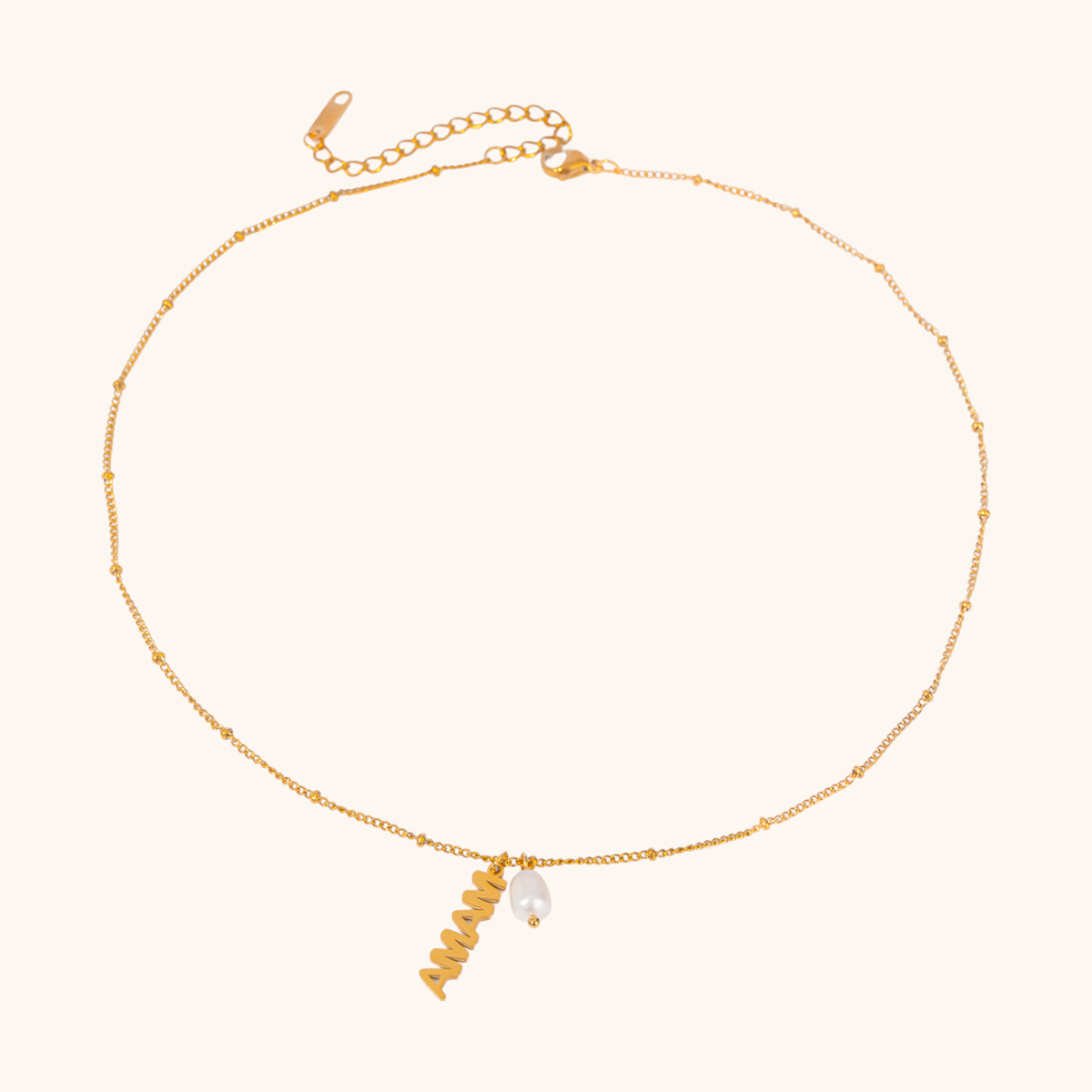 Close-up of gold MAMA letter necklace with pearl charm on a ceramic dish
