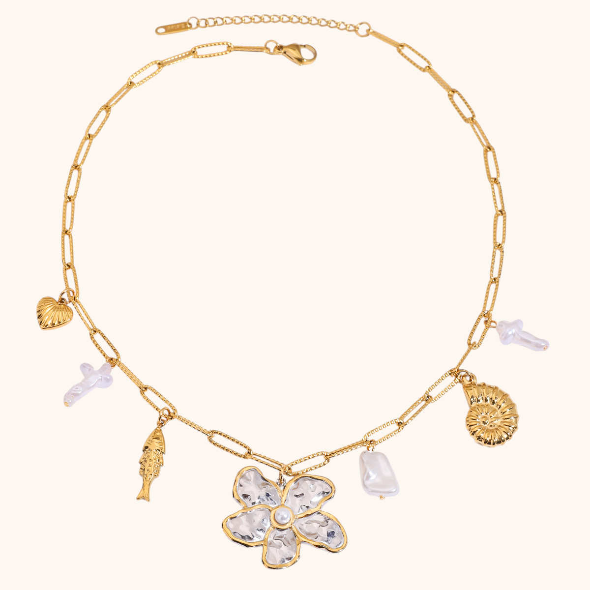 Gold chain necklace with a large hammered flower pendant, shell, and pearl charms on white background