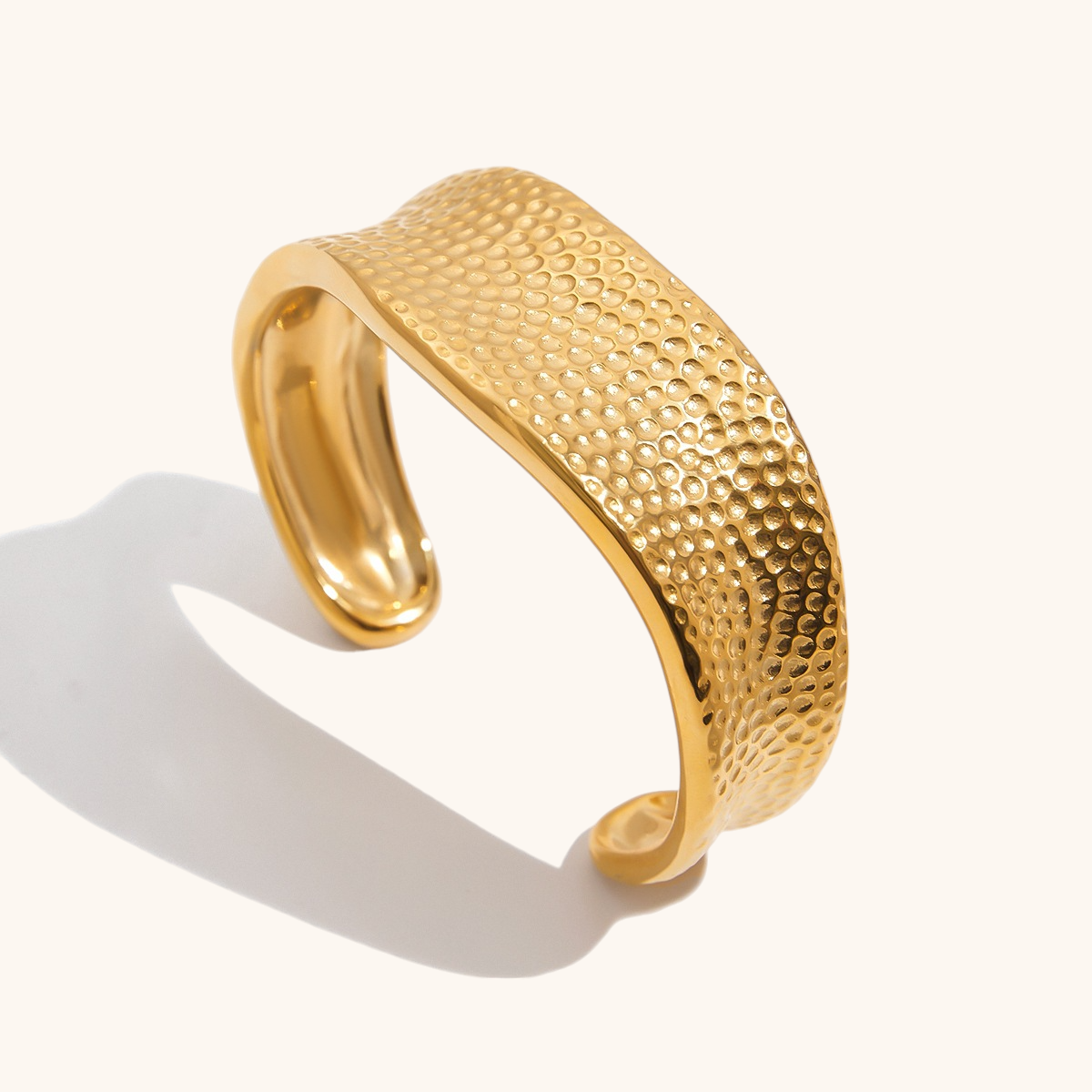 18K gold textured bangle bracelet photographed on a neutral background, showing its curved hammered surface